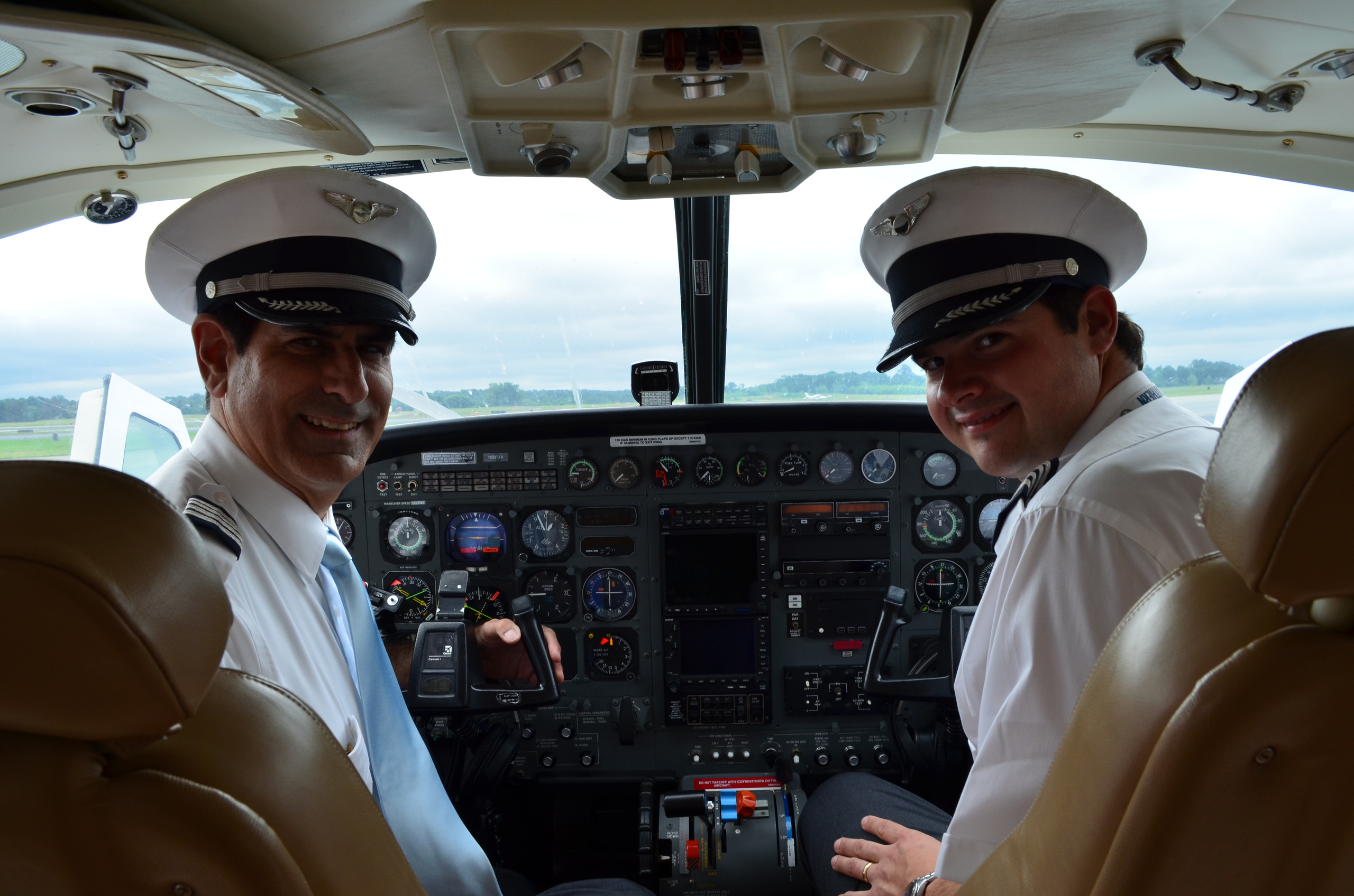Two pilots in a cockpit at Peachtree DeKalb Airport, looking back and smiling at the camera.
